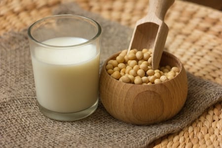 a pot with soyabean along with a glass of soya milk on a brown mat